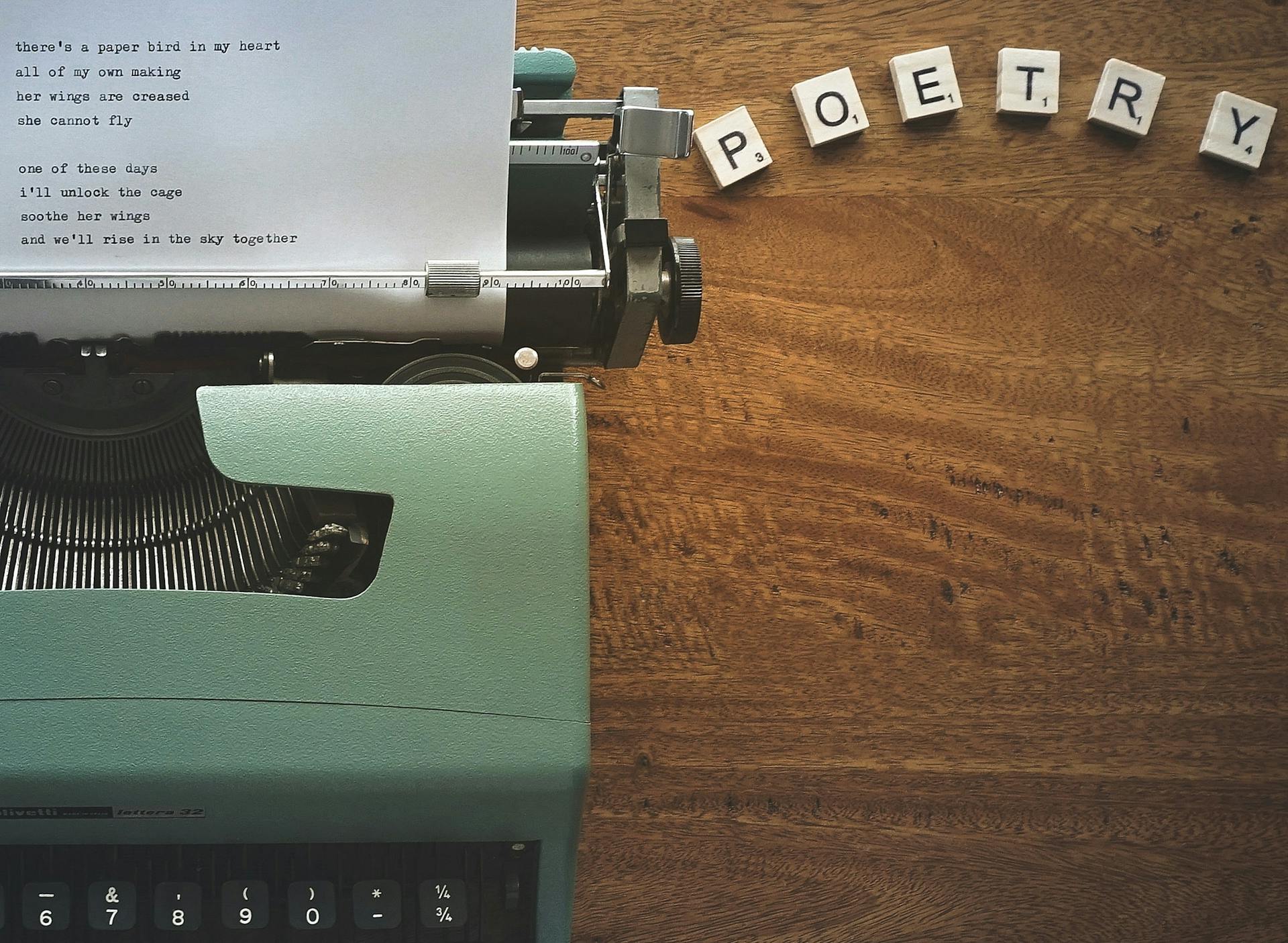 scrabble tiles that spell out the word “poetry” near a typewriter